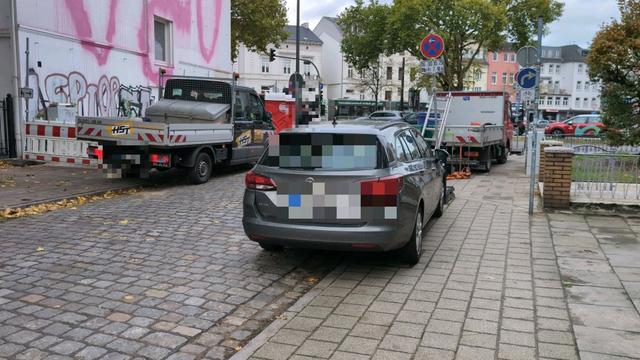 Handwerkerwagen stehen auf dem Gehweg. Auf einer Straßenseite ist der Gehweg zusätzlich direkt neben dem Handwerkerwagen abgesperrt.
