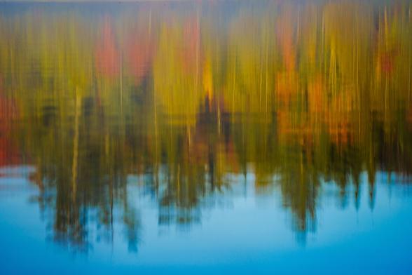 A blurred reflection of colorful trees in calm water, showcasing fall colors.