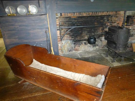 A very large six foot wooden cradle by a colonial era fireplace