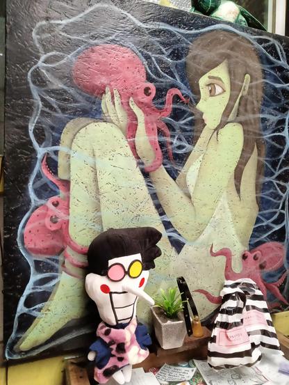 El spamluche podando frente al cuadro de una figura femenina de piel verde sentada sosteniendo y siendo rodeada por pulpos. No hentai pun intended. Spamcito posa como si él lo hubiese dibujado.