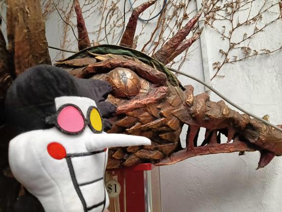 Spamcito posando frente a una cabeza de dragón semi abstracta hecha de madera.