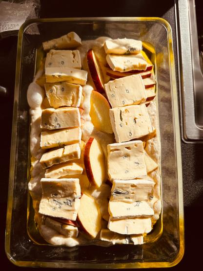 Slices of Gorgonzola and apple are arranged in a baking dish on dough.