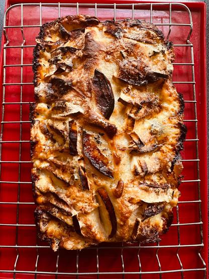 A baked focaccia topped with sliced apples and Gorgonzola is resting on a cooling rack.