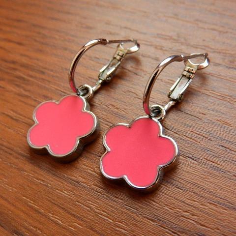 A pair of silver hoop earrings with pink enamel flower-shaped charms, resting on a wooden surface.
