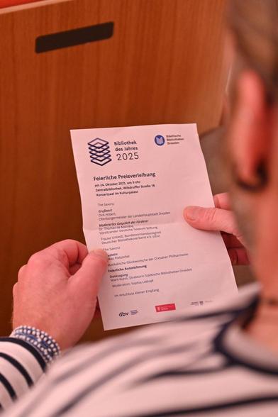 Jemand hält einen aufgefalteten Zettel in der Hand, darauf zu lesen: "Feierliche Preisverleihung"