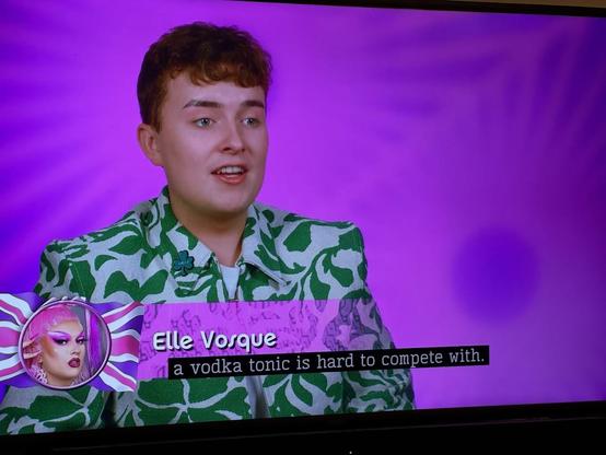 In the Drag Race UK confessional, Elle Vosque, in a green and white top, says "A vodka tonic is hard to compete with."