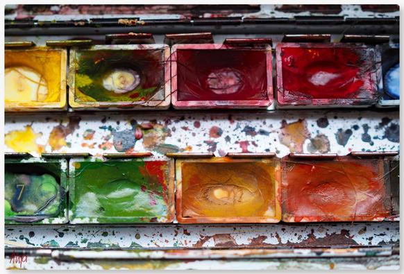 Nahaufnahme eines Farbkastens mit Aquarellfarben in kleinen Kästchen, hauptsächlich Herbstfarben: Gelb, braun, orange, grüne und rote Töne. Die Farben sind zum Teil verbraucht, bunte Spritzer auf dem Boden des Kastens.

Close-up of a paint box with watercolours in small compartments, mainly autumn colours: yellow, brown, orange, green and red tones. Some of the colours have been used up, with colourful splashes on the bottom of the box.