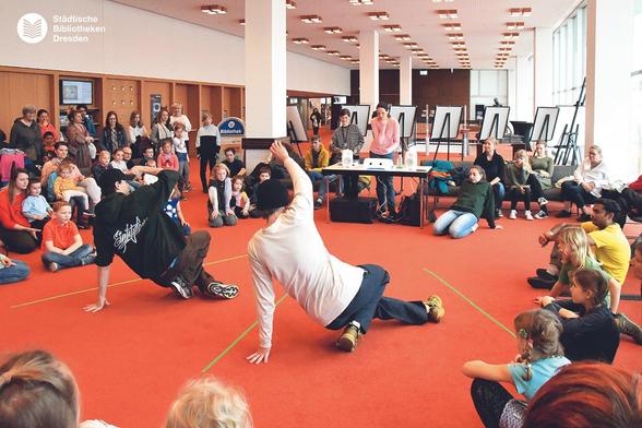 Im Foyer der Bibliothek sitzen Jugendliche um 2 Breakdancer herum.