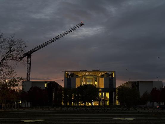 Das deutsche Kanzleramt bei Sonnenuntergang, ein Baukran ragt darüber empor