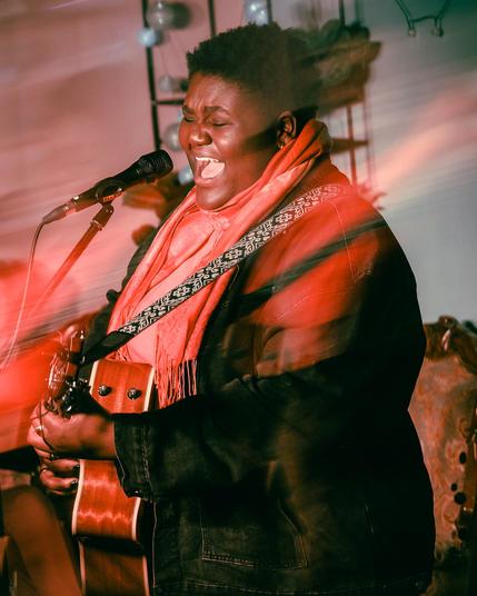 Naomi beim Auftritt - sie hat einen roten Schal und eine schwarze Jacke und singt