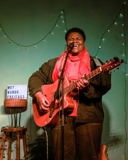 Naomi beim Auftritt - sie hat einen roten Schal und eine schwarze Jacke und singt