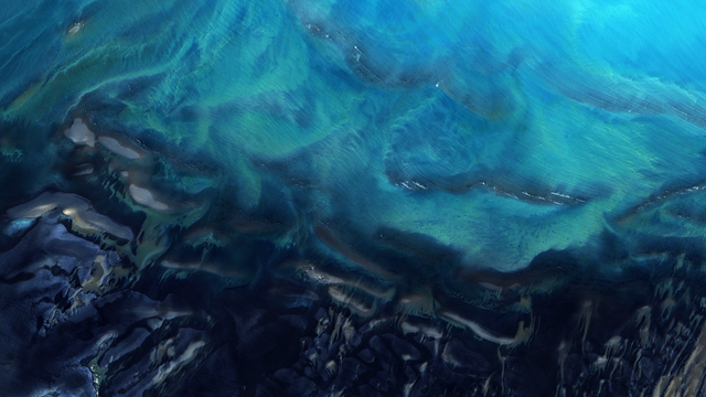 A satellite picture of the seawater on a coastline, with dark blue and teal tones interweaving in abstract patterns.