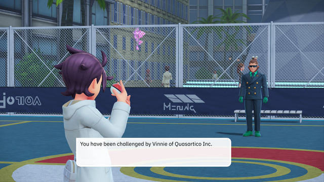 A Pokémon battle challenge screen set in an outdoor urban arena with fencing and distant buildings. On the left stands the player character: a purple-haired trainer in a white coat. On the right is the challenger, Vinnie of Quosartico Inc., wearing a dark double-breasted coat, green gloves, and sunglasses. He stands upright with both arms straight at his sides. On-screen text reads: “You have been challenged by Vinnie of Quosartico Inc.”