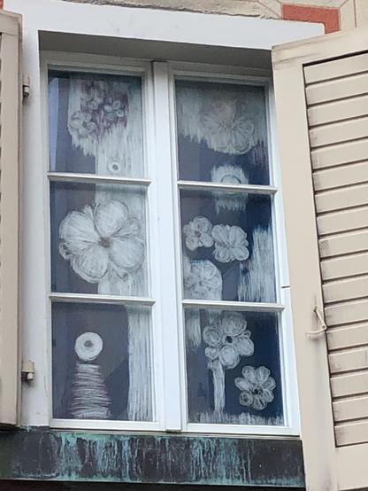 Zwei in drei Teile unterteilte Fensterflügel sind fast vollständig mit weißen Blumen bemalt. Die Künstlerin nahm dazu Kreide. Nun braucht sie weder Gardinen noch Stores.