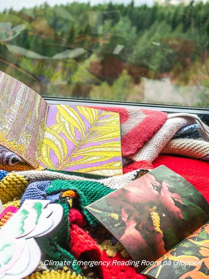 Artists’ books on a bench on carpets in front of a window, with a forest in the background