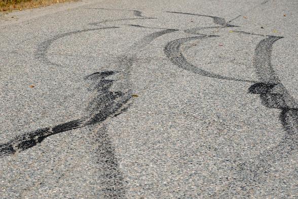 Verschlungene schwarze Bremsspuren auf einer groben Asphalt Strasse. Sieht fast aus wie Graffiti.