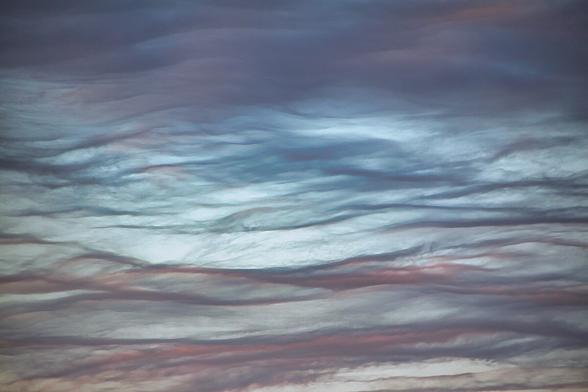 Ein Himmel voller schichtweise angeordneter Wolken in sanften Blau-, Grau- und Rosatönen. Die Formen wirken weich und fließend, wie ruhige Wellen eines luftigen Meeres.