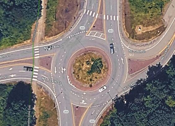 Aerial image of the roundabout at Carnation-Duvall Road NE and NE 124th Street. There are no sidewalks but there is a crosswalk at the north end of the roundabout but nowhere else.