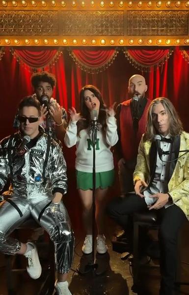 VoicePlay (Layne Stein, Geoff Castelluci, Cesar De La Rosa and Eli Jacobson) dressed in bright colorful clothes, sitting or standing in a theatrical set with rows of lightbulbs and heavy velvet curtains, singing an a capella tune with Rachel Potter (center.)