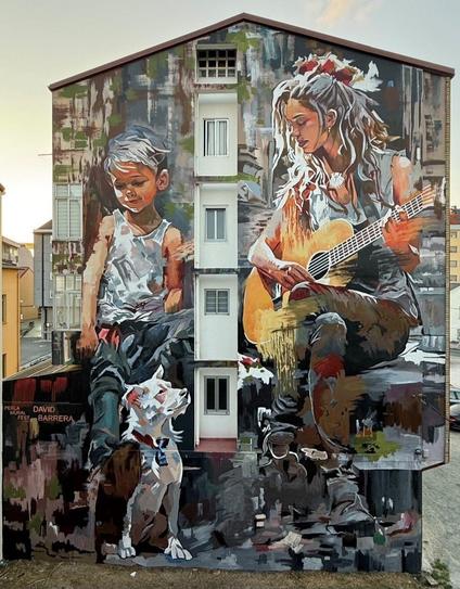 Peinture sur toute la hauteur du mur latéral d'un immeuble de 4 étages. Une femme assise avec une guitare. Regardant un petit garçon aux cheveux plutôt gris que blonds qui se tient debout souriant. Avec à ses pieds son chien assis, blanc et marron, avec un collier. Le style évoque plutôt une vie de bohème et d'art.