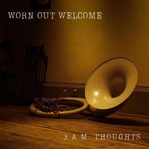 A warm-toned photograph of a brass sousaphone lying on its side on a hardwood floor against a pale yellow wall, with white text overlaid on the image. The instrument rests in the lower right portion of the frame, its flared bell facing toward the viewer and angled slightly upward, catching soft interior light that creates a gentle glow on the bell's interior surface. The horn's coiled tubing and valve mechanism occupy the left side of the composition, with metallic surfaces reflecting muted golden tones from the ambient lighting. The hardwood floor planks run horizontally across the frame, displaying natural wood grain in honey and amber hues. A white baseboard with layered molding runs along the bottom of the wall. On the left side of the frame, the legs of folding chairs are partially visible, appearing dark and silhouetted against the illuminated wall. In the upper left corner, a small framed picture hangs on the wall, though its details remain indistinct in shadow.

Text: WORN OUT WELCOME / 3 A.M. THOUGHTS