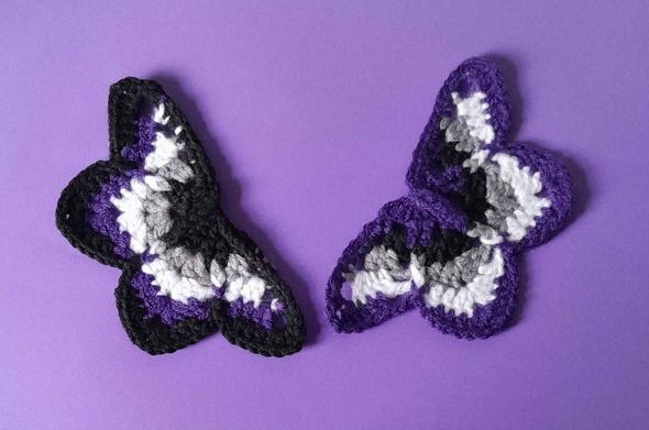 Two crochet moths in Ace Pride Colours (black, grey, white, purple) one with purple as dominat colour one with black