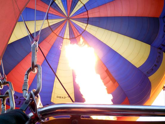 Une flamme puissamment surexposée sort du brûleur d'une montgolfière colorée.