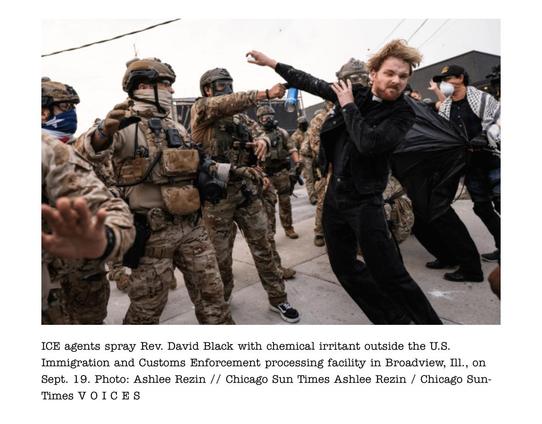 ICE agents in camouflage uniforms confront a man dressed in black, identified as Rev. David Black, outside a U.S. Immigration and Customs Enforcement facility in Broadview, Illinois. One agent sprays a chemical irritant toward him as he recoils, clutching a black umbrella, while others nearby reach out amid the tense scene.