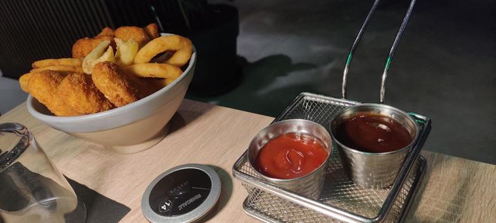 "Tasty bucket" in a bowl filled with fried fake chicken wings + fake chicken nuggets + onion rings and other + two dip sauce containers