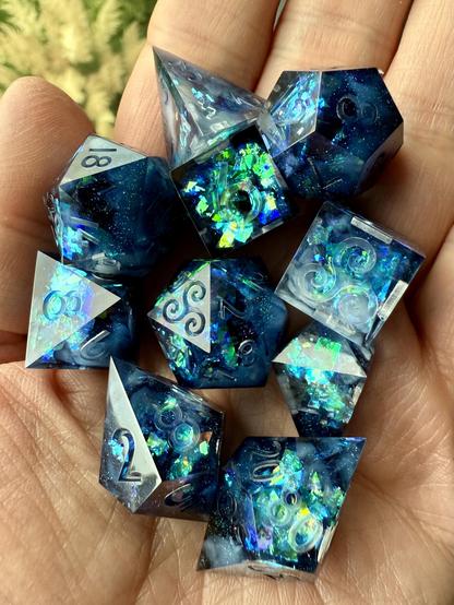 Ein Set Würfel in Blautönen mit glitzernder Folie im Inneren, platziert auf einer Handfläche.