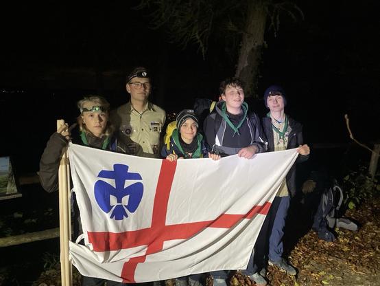 4 Pfadfinder stehen im dunklen mit ihrem Leiter hinter der Fahne der Deutschen Pfadfinder*Innenschaft St.Georg
