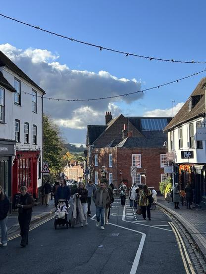 View down a historic high st blue sky in the distance people walking up the hill