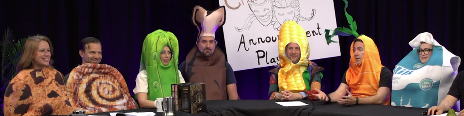 A screenshot from Critical Role
The cast is wearing...ridiculously goofy food costumes.
Marisha seems to be a cookie, Liam seems to be a cinnamon roll, Laura is a pickle, Travis is...maybe a sweet potato? (it's brown with a fleshy top)
Taliesin is a cob of corn, Matt is a carrot, and Ashley is a container of milk