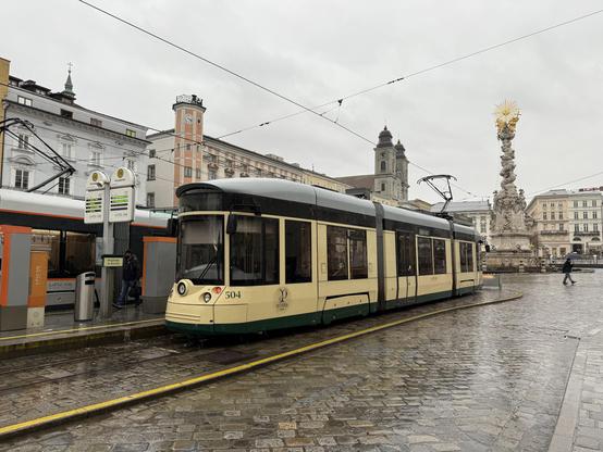 Der Niederflurwagen 504 der Pöstelbergbahn im Stumpfgleis auf dem Hauptplatz im regnerischen Linz. Rechts die Dreifaltigkeitssäule.