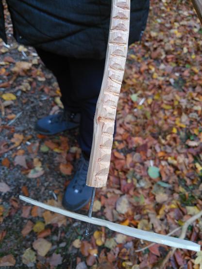 Ein geriffeltes Hölzchen mit einem Propeller vor braunem Herbstlaub. Eine dunkel gekleidete Person im Hintergrund.