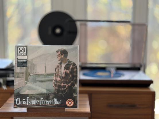 Chris Isaak - Forever Blue LP cover.

Chris, plaid shirt, old car. Artist and title at the bottom.

The blue LP plays on a vintage, restored Bang & Olufsen Beogram 4000 linear-tracking turntable to the right.