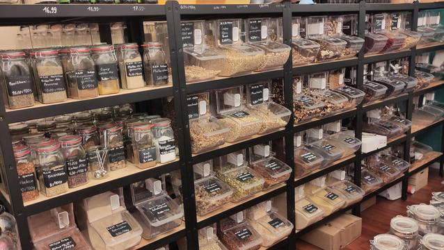 Ein Regal mit Vorratsbehältern mit verschiedenen Nüssen, Müslis, getrocknetem Obst und ahnlichem