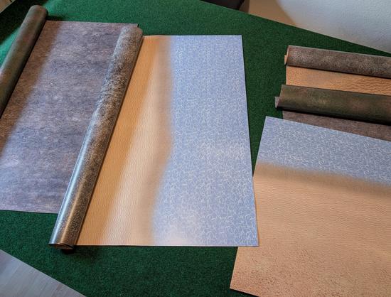 Einige Spielmatten mit unterschiedlichen gedruckten Oberflächen wie Strand, Felsen, Wiese liegen auf einem Tisch.