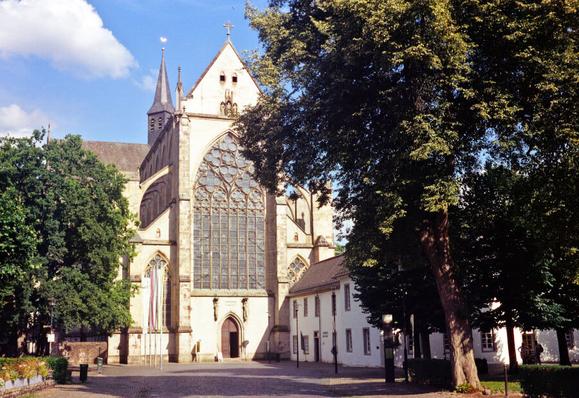A Gothic Abbey with trees in front brightly lit under a blue sky.