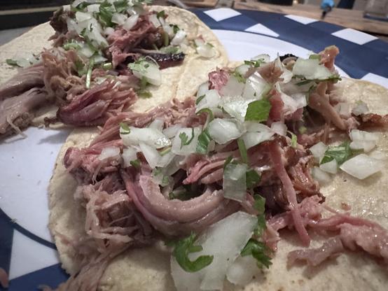 Two tacos filled with pulled meat, topped with chopped onions and cilantro, served on soft tortillas on a blue and white plate.