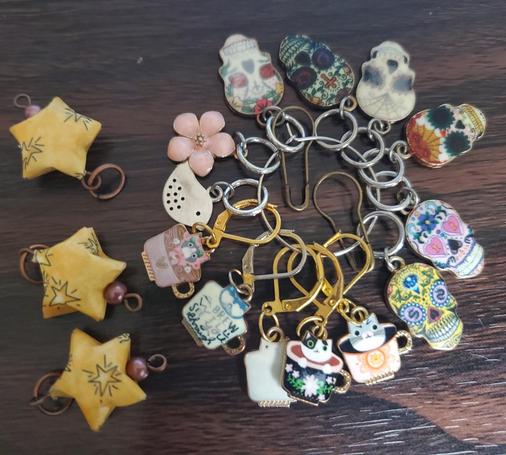 3 stitch markers as tan shaped stars on the left, a circle to the right holding numerous enamel stitch holders