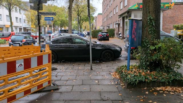 Ein Fahrzeug versperrt komplett eine Fußgängerfurt. Ein ausweichen auf in die Kreuzung wird für Rollatoren, Kinderwägen, Rollstühle usw. durch eine Baustellenabsperrung verhindert.