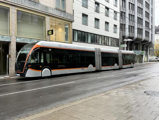 Auf der gegenüberliegenden Seite der Straße steht ein O-Bus mit gesenktem Stromabnehmer.