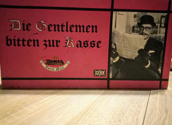 Die rote Verpackung mit dem Namen des Spiels und dem schwarzweiß Foto eines jungen Horst Tappert (aka Derick - leider Nazi) mit Bowler auf dem Kopf und Zeitung in der Hand. Sehr englisch. Passend, da es um den großen Postraub geht.