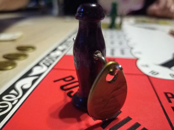 Ein dunkellila Meeple, an dessen "Armhaken" ein Geldsack hängt.