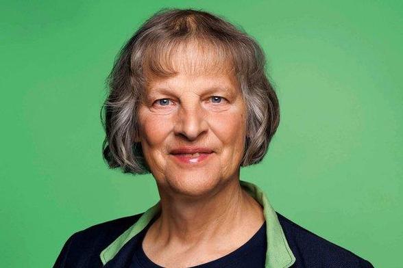 Diana Siebert, Porträtfoto vor grünem Hintergrund. Sie trägt eine graue Bob-Frisur und ein dunkles Oberteil mit grünen Akzenten am Kragen, sie lächelt freundlich in die Kamera.