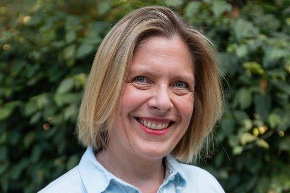 Anne Roth, Bezirksvertreterin, Porträtfoto in hellblauem Hemd vor grünem Blätterhintergrund. Sie trägt ihre blonden Haare seitlich gescheitelt und lächelt in die Kamera.
