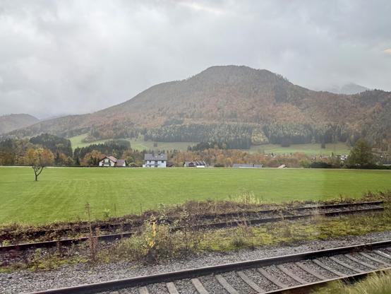 Blick durch ein Zugfenster auf eine Herbstlandschaft in den Alpen, die bereits stark fortgeschritten ist.