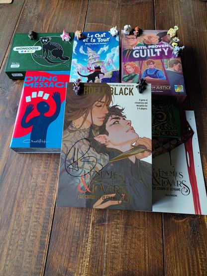 5 card games and board games: Mongoose (cover: a mongoose), Le chat et la tour (cover: a small black cat climbing up a tower), Until Proven Guilty: thirst for justice (cover: a young bespactacled male lawyer doing an "objection!" finger gesture), dying message (cover: stylized murder victim with 4 cards), Holly Black: Enemies &amp; Lovers the crown of Elfhame (cover: a young woman holding a dagger to a handsome fae prince's throat with gold foil accents). There is also a set of 11 tiny toy animals and baby dragons scattered all over the game boxes.