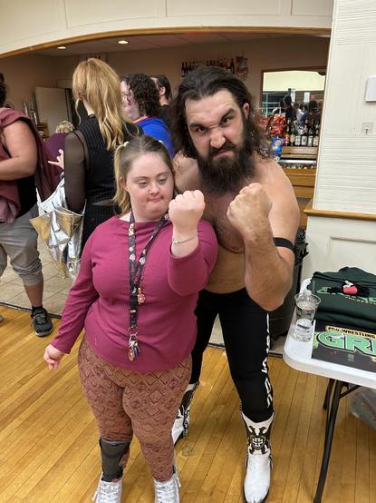 A young woman with Down syndrome mimics the pose of a pro wrestler who is standing next to her holding up his fist.